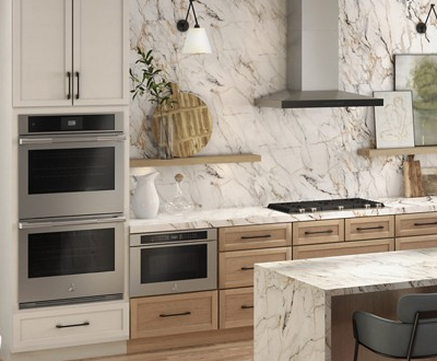 A kitchen with a JennAir Double Wall Oven, a JennAir Microwave and a JennAir Cooktop under a JennAir Over-the Range Hood. There's also an island with a chair. On the counter is a vase and other items. On a shelf is a potted plant. 